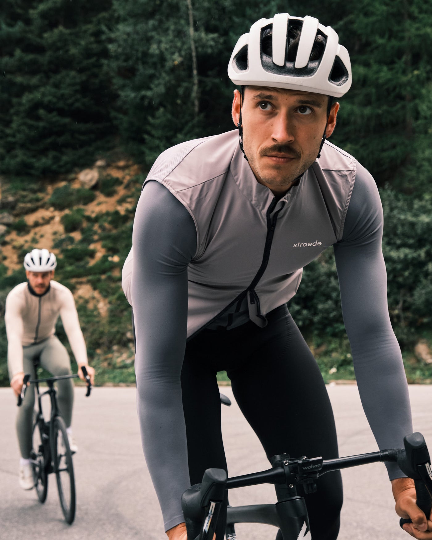 Zwei Rennradfahrer hintereinander. Der erste trägt ein Langarm-Shirt und darüber eine Rennradweste.