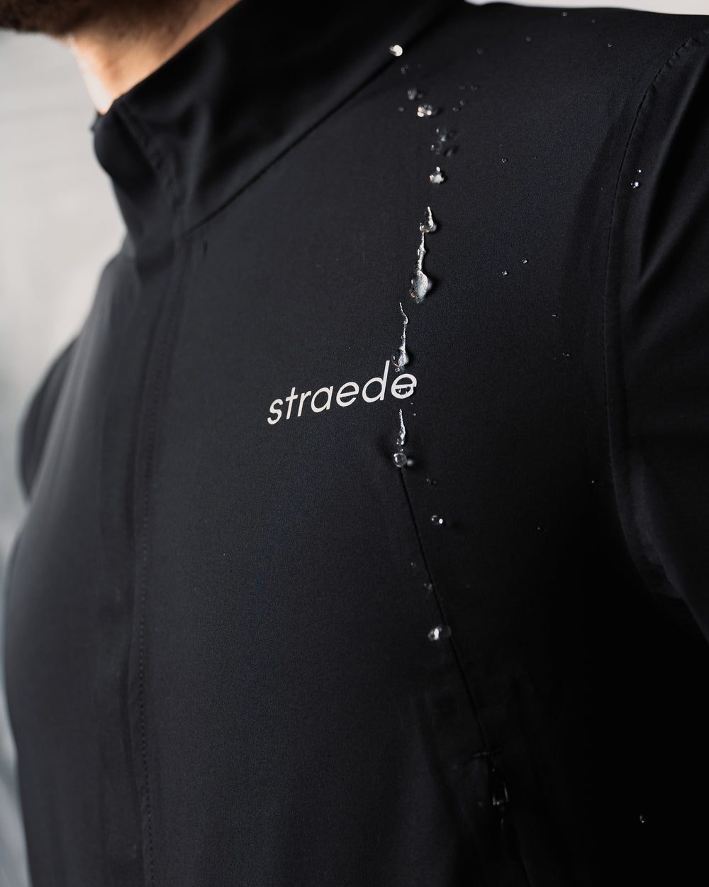 #farbe_black | winddichte Regenjacke für Herren in schwarz Nahaufnahme Straede-Aufdruck auf der Brust